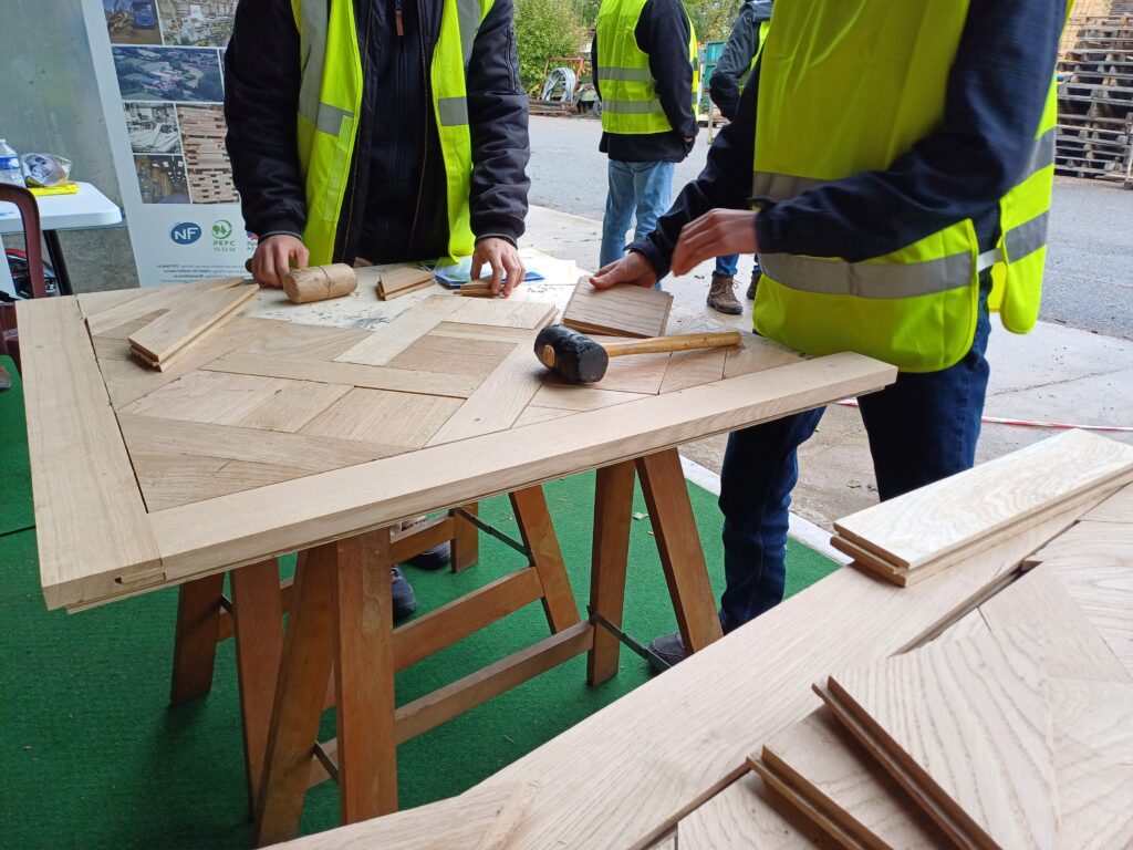 Gros plan sur les mains de 2 élèves de 3èmes qui s'essaient à la mise en place d'un panneau de parquet versaillais. Il y a des maillets en caoutchouc et des bouts de bois découpés
