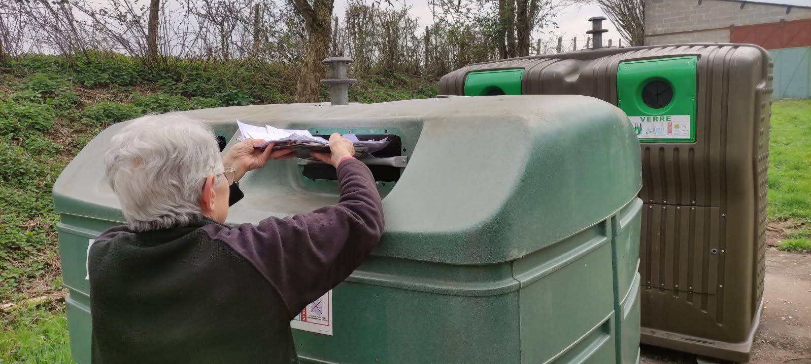 Une dame met des papiers dans le conteneur à papier, en passant au-dessus d'une barre.